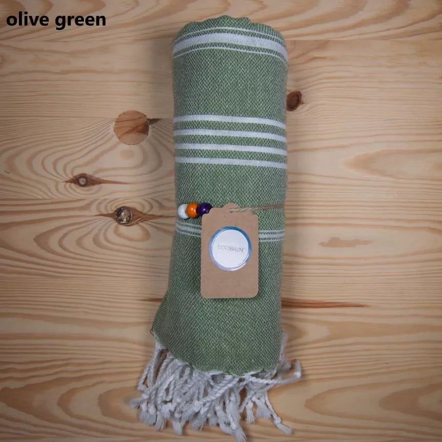 Zusammengerolltes Badetuch in der Farbe olive green für den Strand auf Holzhintergrund