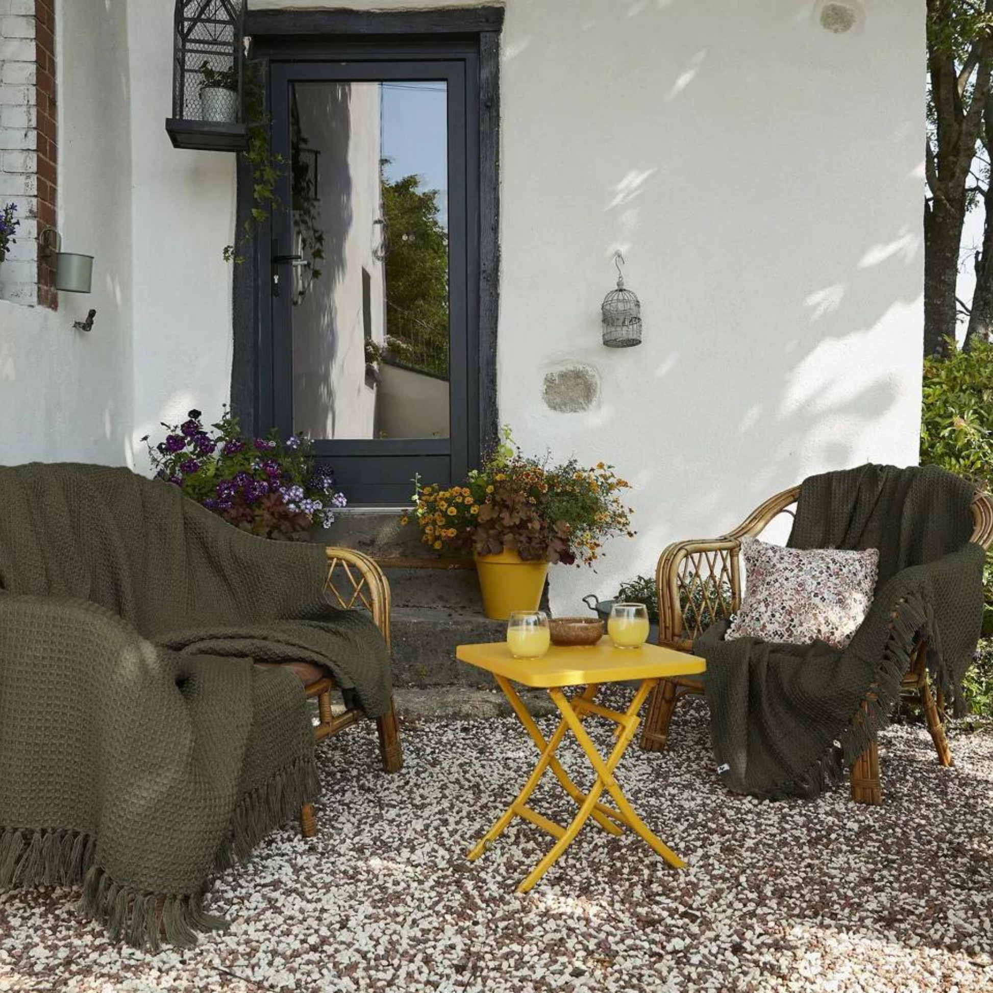 Terrasse mit einer Bank und Stuhl auf denen eine grüne Fransendecke liegt